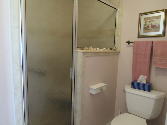 bathroom featuring a shower with shower door and toilet