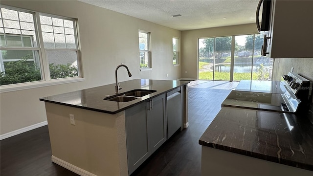 kitchen with dark stone countertops, a kitchen island with sink, dark hardwood / wood-style floors, range with electric stovetop, and sink