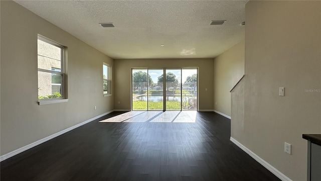 empty room with a textured ceiling, a wealth of natural light, and dark wood-type flooring