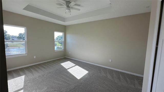 carpeted spare room with ceiling fan and a raised ceiling