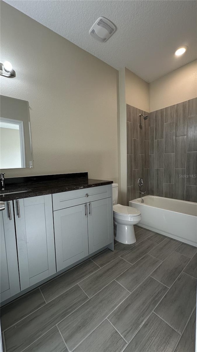 full bathroom with toilet, tile floors, tiled shower / bath, vanity, and a textured ceiling