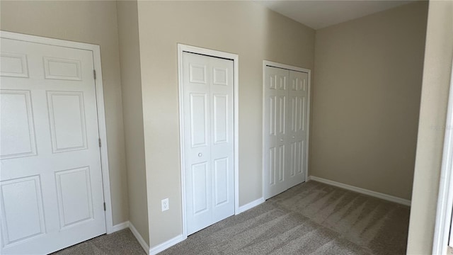 unfurnished bedroom featuring dark colored carpet and multiple closets