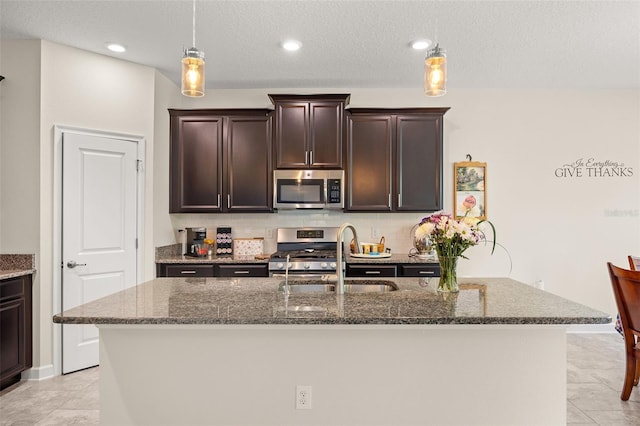 kitchen with dark stone countertops, a kitchen island with sink, gas range oven, dark brown cabinetry, and light tile floors