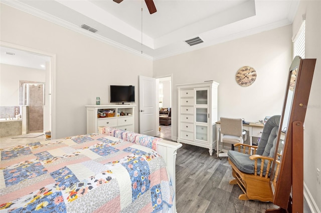 bedroom with ceiling fan, a tray ceiling, ornamental molding, wood-type flooring, and ensuite bath