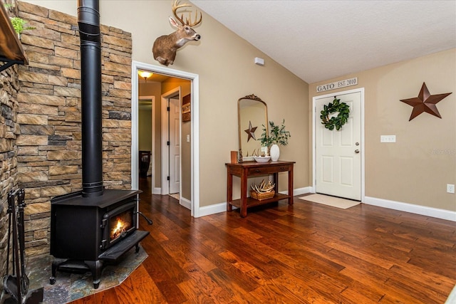 entrance foyer featuring dark hardwood / wood-style flooring, vaulted ceiling, and a wood stove