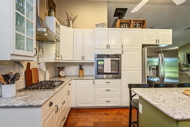 kitchen with white cabinetry, dark hardwood / wood-style floors, stainless steel appliances, light stone countertops, and wall chimney range hood