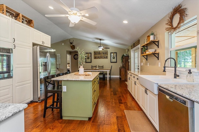 kitchen featuring vaulted ceiling, a kitchen island, appliances with stainless steel finishes, a breakfast bar, and sink