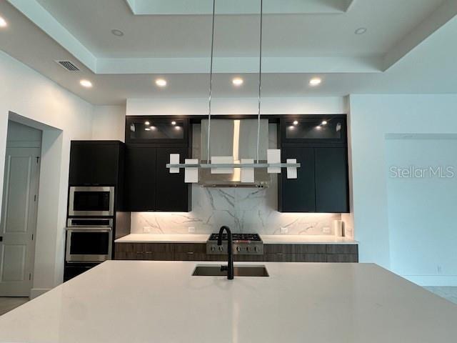 kitchen with stainless steel appliances, decorative backsplash, a tray ceiling, wall chimney exhaust hood, and sink