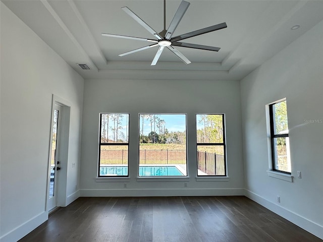 empty room with a raised ceiling, a wealth of natural light, and dark hardwood / wood-style flooring