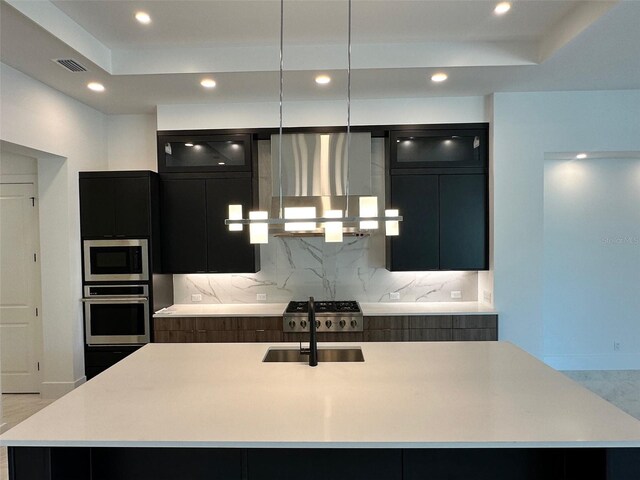 kitchen with a kitchen island with sink, backsplash, stainless steel appliances, and wall chimney exhaust hood