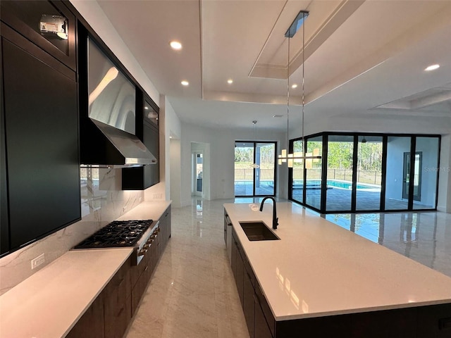 kitchen featuring sink, a spacious island, a tray ceiling, stainless steel gas cooktop, and decorative light fixtures