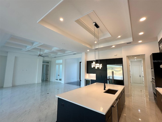 kitchen featuring sink, built in refrigerator, decorative light fixtures, a tray ceiling, and a large island