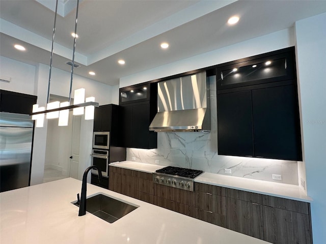 kitchen with sink, wall chimney range hood, backsplash, stainless steel appliances, and decorative light fixtures