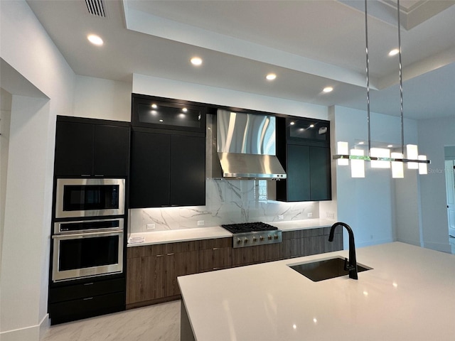 kitchen with sink, decorative light fixtures, appliances with stainless steel finishes, decorative backsplash, and wall chimney range hood