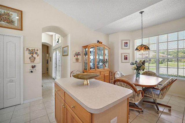 kitchen with a textured ceiling, a center island, hanging light fixtures, and light tile patterned flooring