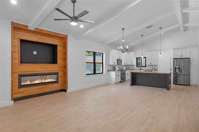 kitchen with a large fireplace, a kitchen island, white cabinetry, beamed ceiling, and appliances with stainless steel finishes