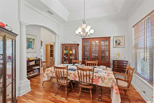 dining area with a raised ceiling, an inviting chandelier, decorative columns, and light wood-type flooring