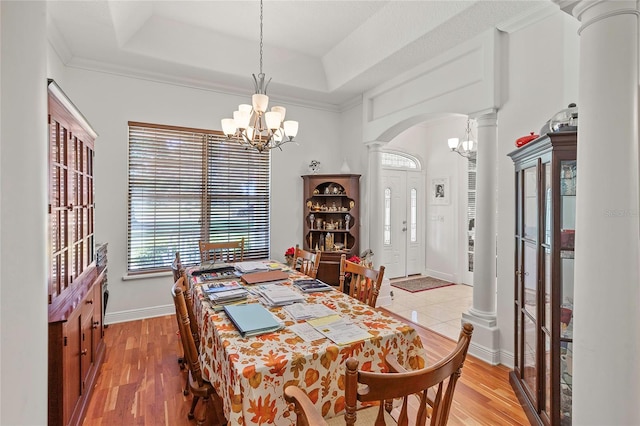 dining area featuring a notable chandelier, a raised ceiling, light hardwood / wood-style flooring, and decorative columns