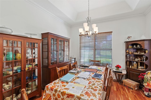 dining room featuring a notable chandelier, a raised ceiling, crown molding, and wood-type flooring