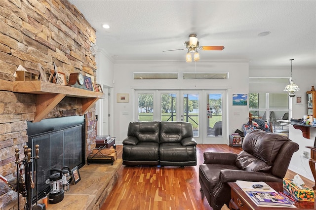 living room featuring a textured ceiling, ceiling fan, hardwood / wood-style floors, and a stone fireplace