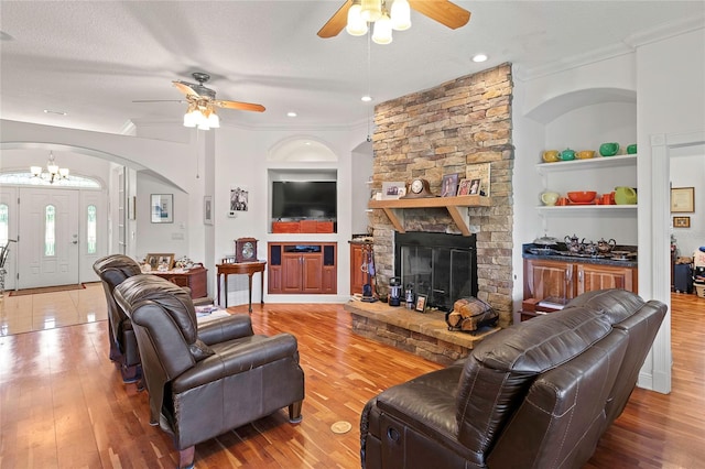 living room with built in shelves, a fireplace, a textured ceiling, ceiling fan with notable chandelier, and hardwood / wood-style flooring