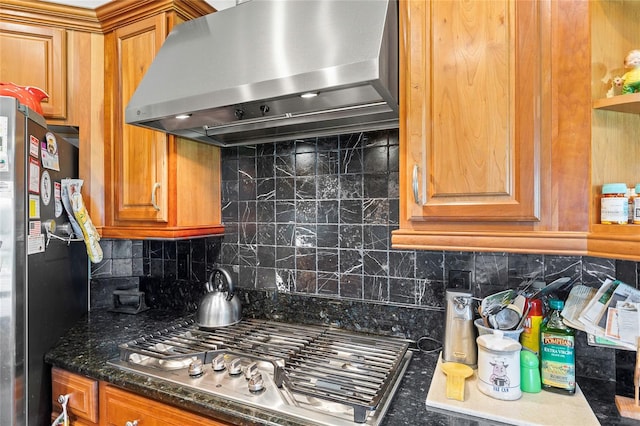 kitchen with wall chimney range hood, stainless steel appliances, decorative backsplash, and dark stone counters