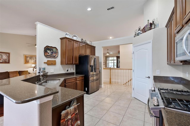 kitchen featuring light tile patterned floors, kitchen peninsula, stainless steel appliances, dark stone countertops, and sink