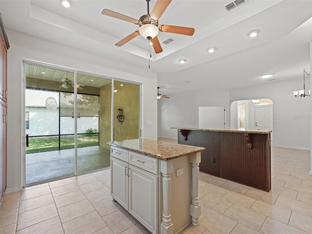 kitchen featuring a tray ceiling, a center island, light stone countertops, and white cabinets