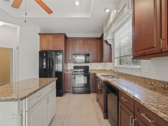 kitchen with a tray ceiling, light stone countertops, sink, and black appliances