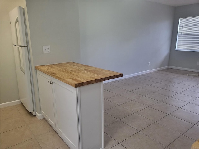 kitchen featuring white refrigerator, butcher block countertops, white cabinetry, and light tile floors