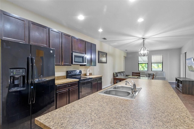 kitchen featuring sink, black appliances, a notable chandelier, hanging light fixtures, and an island with sink