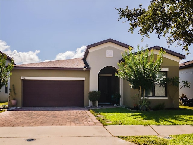 view of front of house featuring a garage, decorative driveway, a front lawn, and stucco siding