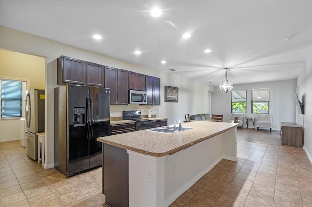 kitchen featuring stainless steel appliances, sink, light tile patterned floors, hanging light fixtures, and an island with sink