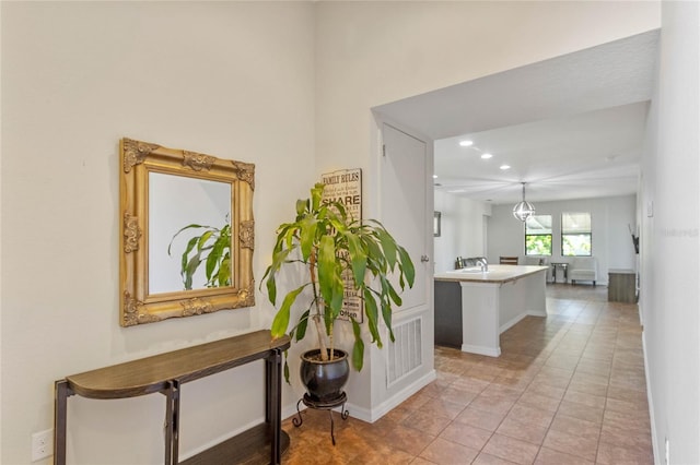 hallway with recessed lighting, a sink, baseboards, and light tile patterned floors