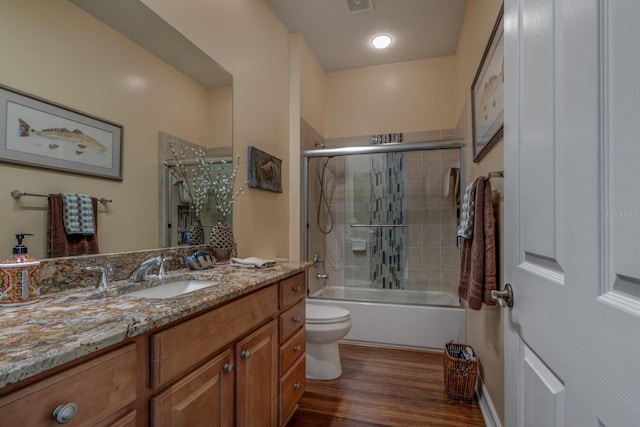 full bathroom with shower / bath combination with glass door, hardwood / wood-style floors, vanity, and toilet