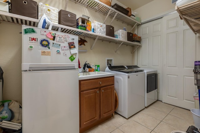 laundry area with separate washer and dryer, light tile patterned floors, and cabinets