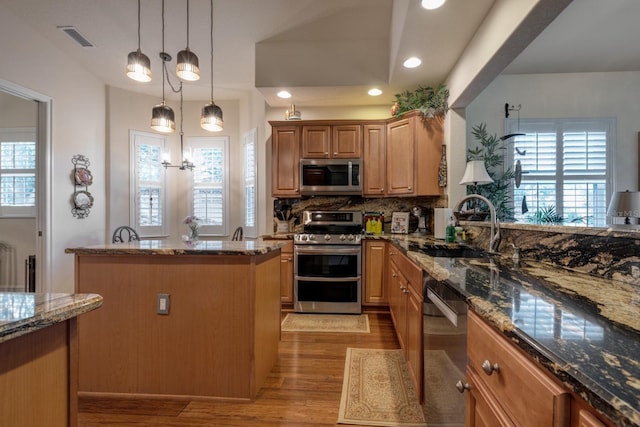 kitchen with pendant lighting, sink, dark stone countertops, appliances with stainless steel finishes, and a kitchen island