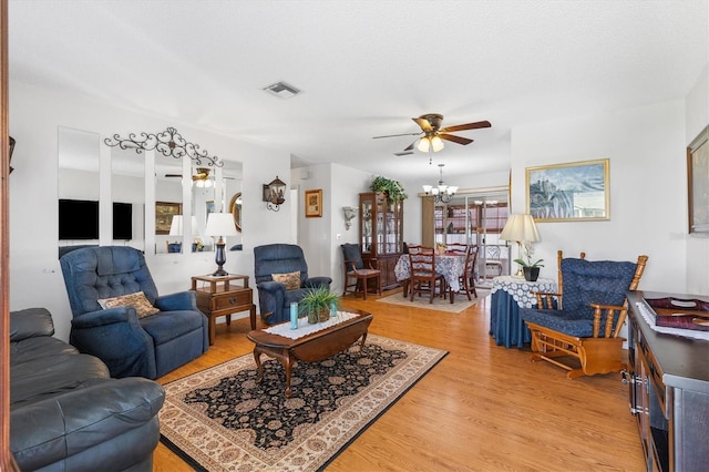 living room with ceiling fan with notable chandelier and light hardwood / wood-style flooring