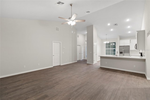 unfurnished living room with sink, high vaulted ceiling, dark wood-type flooring, and ceiling fan with notable chandelier