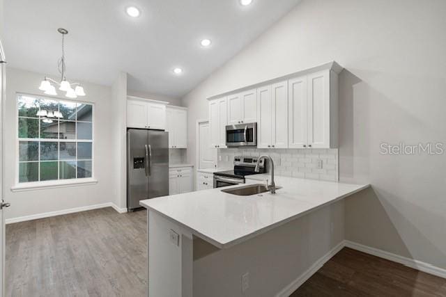 kitchen featuring kitchen peninsula, stainless steel appliances, sink, white cabinetry, and hanging light fixtures