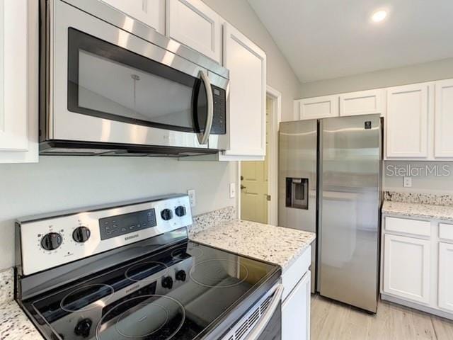 kitchen featuring stainless steel appliances, vaulted ceiling, white cabinetry, and light hardwood / wood-style flooring