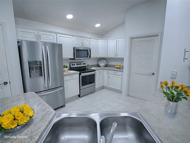 kitchen with stainless steel appliances, sink, light tile patterned floors, white cabinets, and lofted ceiling