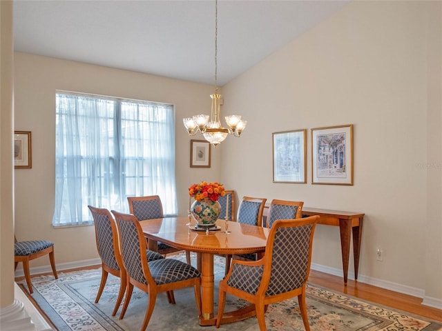 dining space with hardwood / wood-style flooring, lofted ceiling, a wealth of natural light, and an inviting chandelier