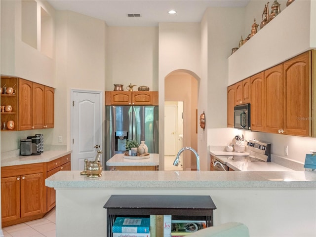 kitchen with a high ceiling, sink, light tile patterned flooring, kitchen peninsula, and stainless steel appliances