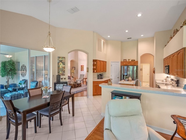 kitchen with high vaulted ceiling, light tile patterned floors, appliances with stainless steel finishes, decorative light fixtures, and kitchen peninsula