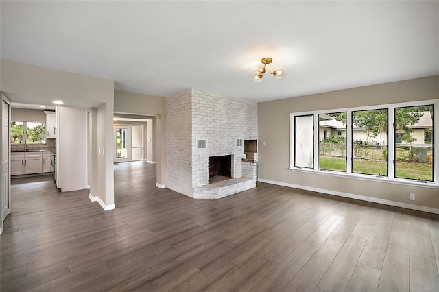 unfurnished living room with sink, dark wood-type flooring, a chandelier, and a brick fireplace