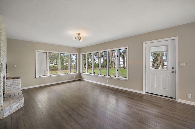 unfurnished living room with a healthy amount of sunlight, dark hardwood / wood-style floors, a brick fireplace, and a notable chandelier