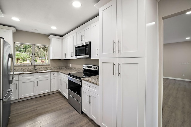 kitchen with sink, hardwood / wood-style flooring, appliances with stainless steel finishes, light stone counters, and white cabinetry