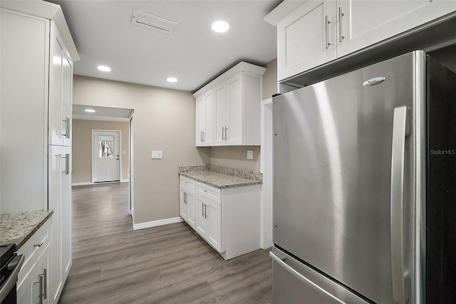 kitchen featuring stainless steel refrigerator, light stone counters, and white cabinets