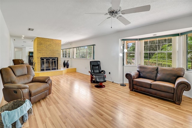 living room featuring a textured ceiling, ceiling fan, light hardwood / wood-style floors, and a fireplace